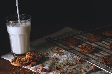 Still life of chocolate cookies and glass of milk on a dark wooden table, adorned with oven rack, cotton dishcloth. Photography in low key and rustic style.