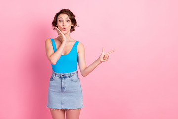 Photo of charming lovely shocked young girl hand cheekbone amazed directing finger empty space amazed shop opening wear denim mini skirt blue tank-top isolated pink color background