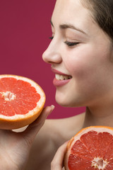 Portrait of an attractive girl holding a sliced ​​slice of grapefruit on a red background.