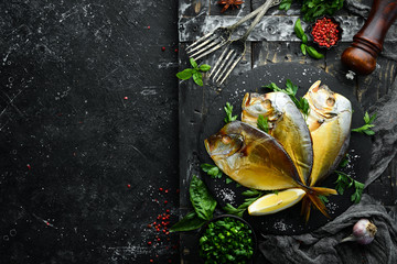 Smoked sea fish Vomer with parsley on a black stone plate. Top view. Free space for your text.