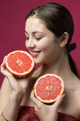 Portrait of an attractive girl holding a sliced ​​slice of grapefruit on a red background.