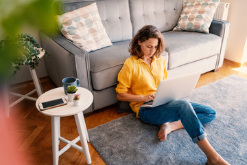 Beautiful young girl woman in yellow shirt works on laptop at home in living room sitting on floor