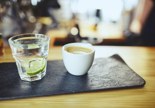 Blurred image of stone plate with cup of coffee and water in a glass with lime on bar counter.Coffee break 