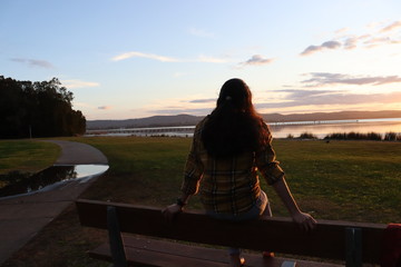 Silhouette of a girl sitting on a bench park watching the sunset.
