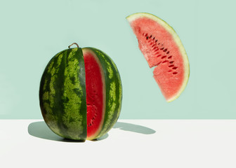 A large fresh watermelon and a levitating red watermelon slice on a neo mint background. Creative...