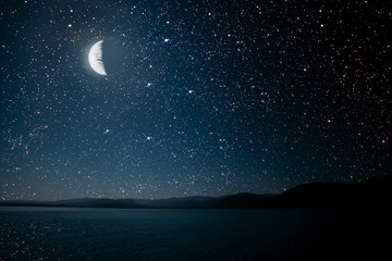 moon against a bright night starry sky reflected in the sea.