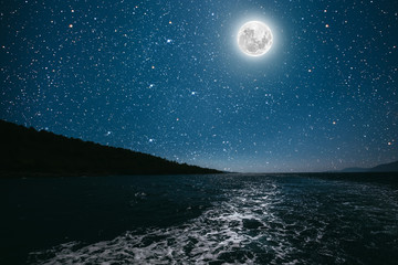 moon against a bright night starry sky reflected in the sea.