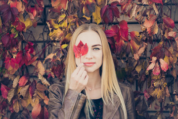 Pretty woman with autumn leaves. The girl closing face the autumn leaf in the park. Concept of good mood at the autumn time
