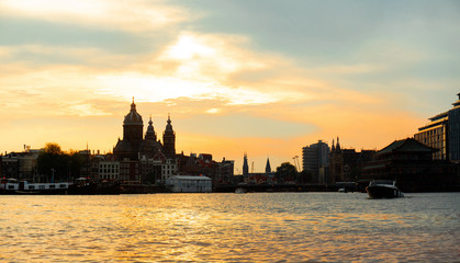 Fototapeta premium Canal in Amsterdam with pleasure boat and historic buildings. View from boat in sunset.
