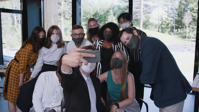 COVID-19 safety lifestyle. Happy young diverse workplace colleagues posing for selfie photo in face masks at office.