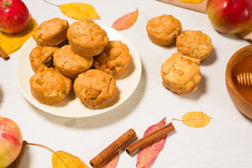 autumn baking concept with seasonal apples and cinnamon honey. Apple cupcakes and muffins on a plate top view on a light background with autumn yellow leaves.