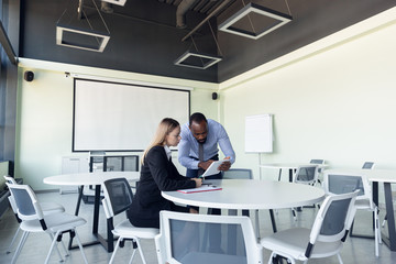 Obraz premium Young businessman waiting for departure in airport, work trip, business lifestyle. Man and woman with gadgets before starting their vacation, registration. Working in special waiting zone together.