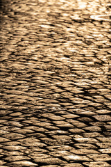 Kopfsteinpflaster, Stra&szlig;enbelag aus Naturstein im Verband gelegt, gl&auml;nzt im Abendsonne Gegenlicht.
