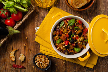 Traditional Italian caponata, served with croutons in a yellow, sunny pot. Decorated with basil and pine nuts.