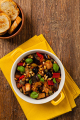 Traditional Italian caponata, served with croutons in a yellow, sunny pot. Decorated with basil and pine nuts.