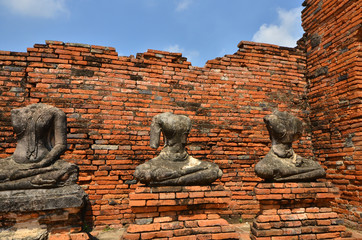 Headless Buddha images on the bases beside red brick wall