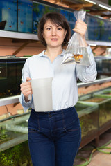 Portrait of happy young woman with goldfish for home aquarium in petshop..