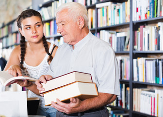 Old man with girl are choosing science-fiction in bookstore.