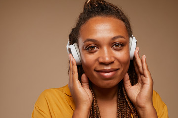 Close-up of African woman wearing wireless headphones looking at camera and listening to music