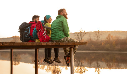 Happy travelers with backpacks resting near river