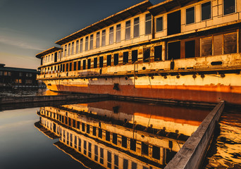An abandoned ship is on the water. The reflection on the water. Sunset.