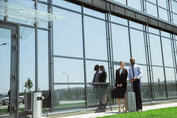 Presentation. Meeting of young business partners after arriving to end point of business trip. Man and woman walking against glass wall background of modern building. Concept of business, finance, ad.