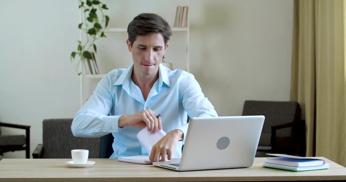 Man office worker freelancer sits at table, dancing actively moving to music writes notes, makes mistake, tears out paper, destroys in small pieces, throws in air, turns on chair, fools in workplace