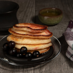 Several pancakes with black currant berries on wood background.