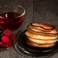 Several pancakes with berries and a cup of tea on wood background.