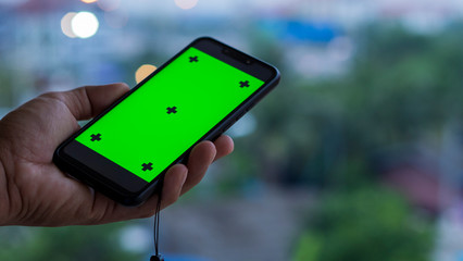 A man's hand holding a smartphone with a green screen is used for multimedia editing.