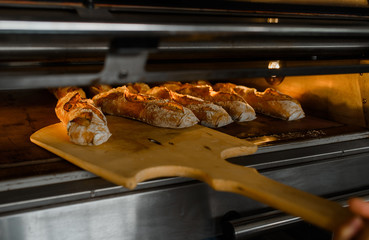 Close up of baker is taking off from oven the french baguette bread with wood peel at baking manufacture factory