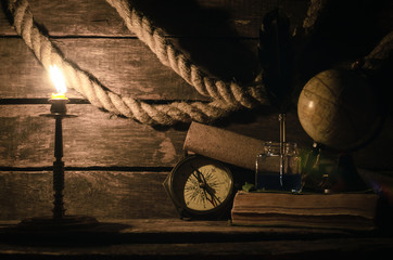 Sea travel background. Adventure background. Globe, compass, mooring rope, scroll map, quill pen in inkpot diary book and burning candle on a wooden captain table.