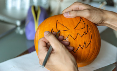 Person carving a pumpking with scary face. Preparing jack o lantern for halloween