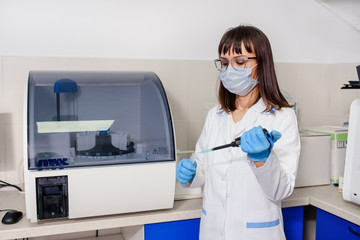Young woman doctor laboratory assistant is using a micropipette test tubes near a fully-automated...