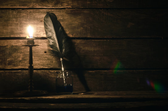 Quill pen in a inkpot and burning candle on the writer desk table background with copy space. Education concept.