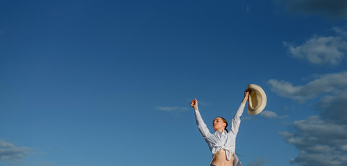 Young woman holding a hat and feel free on a blue sky with clouds background