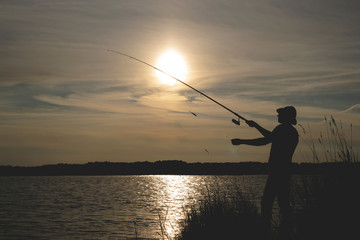 Fisherman silhouette with a rod on the pond.