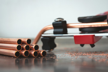 Pipe bender tool and a brass pipes on a workbench of fitter background.