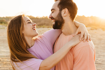 Image of young caucasian happy couple smiling and hugging by seaside