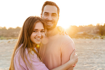 Image of young caucasian happy couple smiling and hugging by seaside