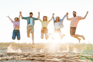 Obraz premium Image of young people holding their hands and jumping together on beach