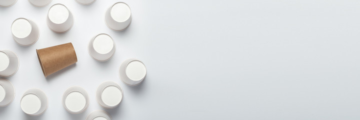 Many white and one brown paper cups, flipped upside down on a light background. Top view, flat lay. Banner