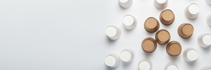 White and brown paper cups flipped upside down on a light background. Top view, flat lay. Banner