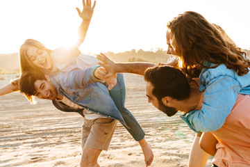 Image of young people piggybacking together on beach in summertime