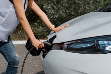 Close up hands holding a power cable and charging the battery of an electric car.