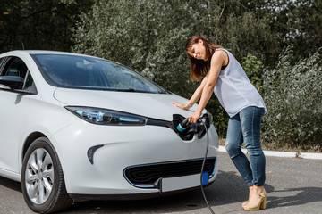 Fototapeta na wymiar Young beautiful woman is charging her electric car at the charging station situated in the forest.