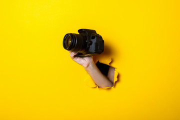 Female hand holding a camera on a bright yellow background