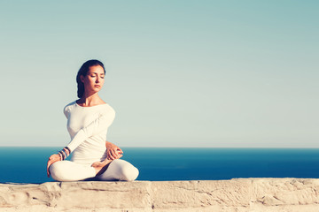 Fototapeta na wymiar Front portrait of gorgeous young woman practicing yoga on a sunny day with amazing sea horizon on background, woman seeking enlightenment through meditation,relaxed girl performing yoga routine,filter