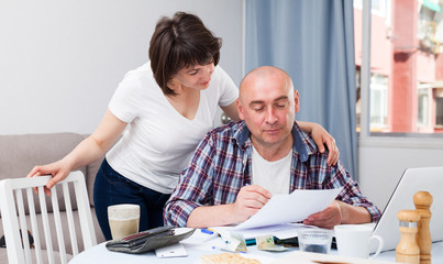 Obraz premium Smiling wife taking care of husband working at home with laptop. High quality photo