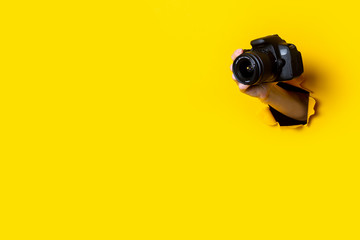 Female hand holding a camera on a bright yellow background